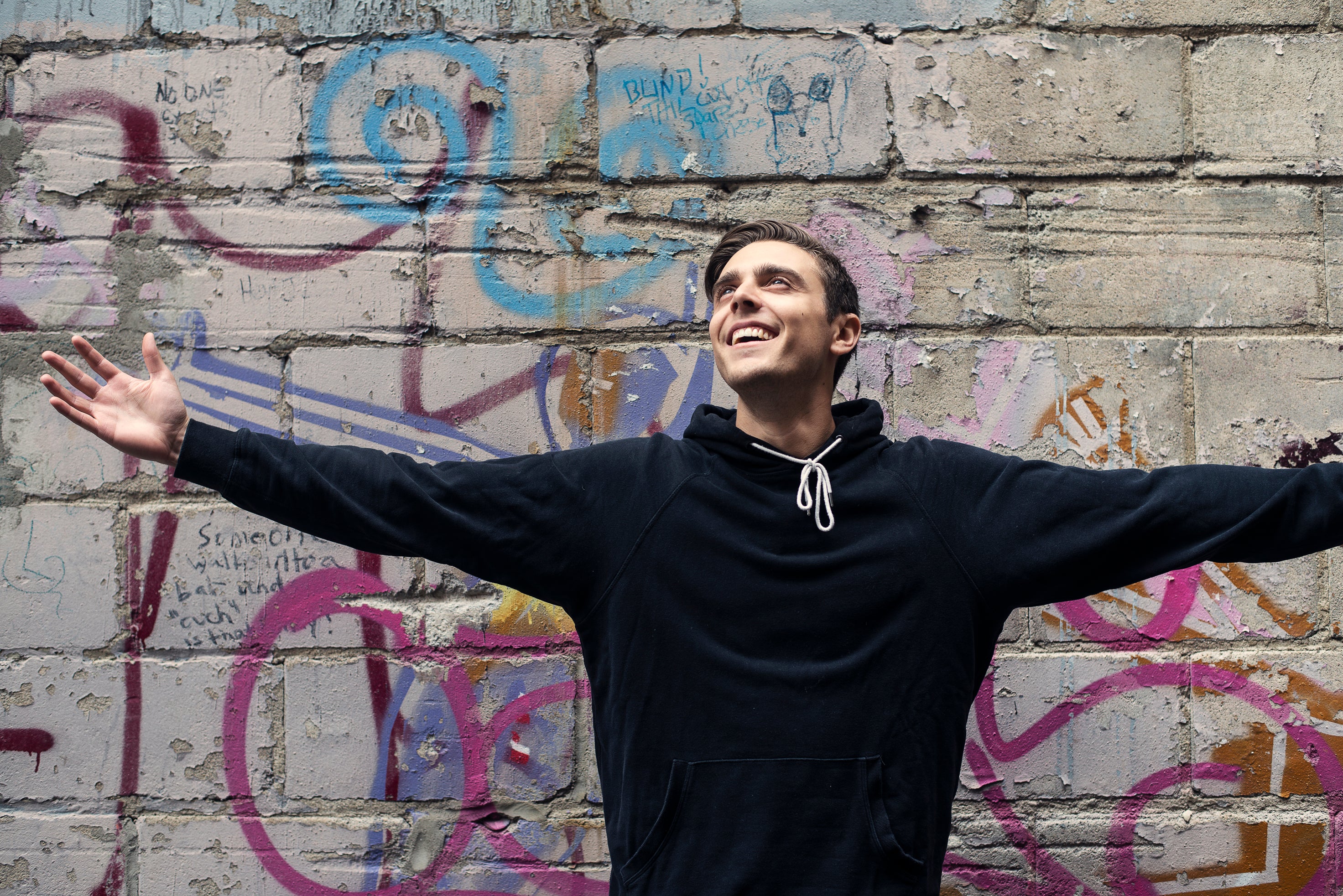 man-smiles-with-open-arms-in-city